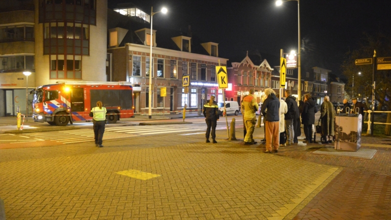 Een nachtelijke scène met een brandweerwagen en mensen, waaronder politie en een brandweerman, staande op een kruispunt.