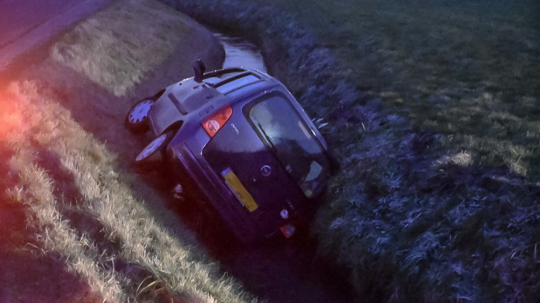 Auto gekanteld in een sloot langs een landelijke weg.