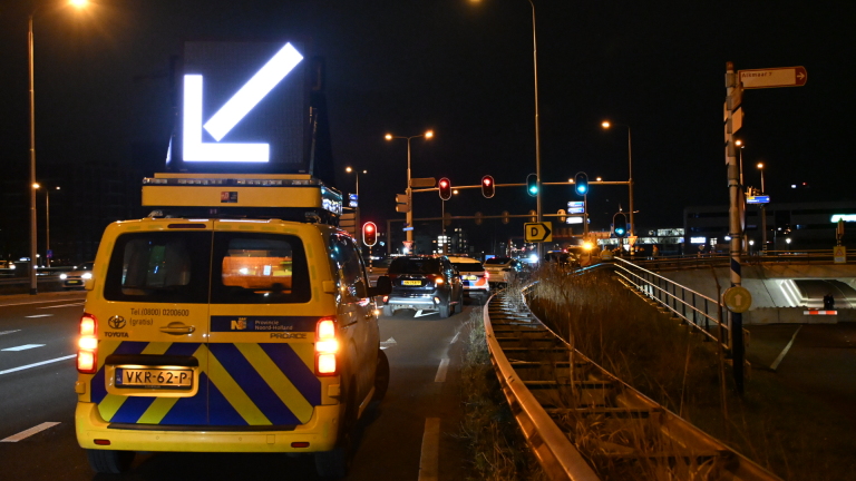 Auto met schade aan de voorkant op een weg 's nachts, met een politieagent en een verkeerskegel in de achtergrond.
