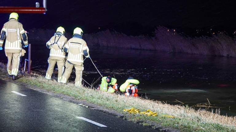 Hulpverleners werken 's nachts in de regen bij een ongeval langs de weg met een ambulance en brandweervoertuigen.