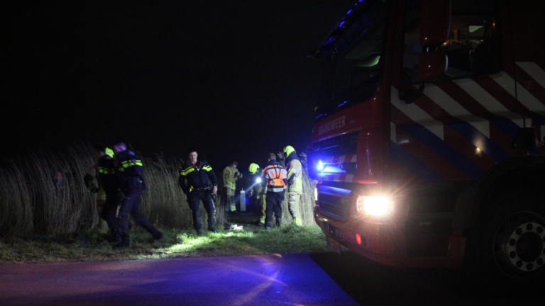 Brandweerlieden op een reddingsboot uitvoeren een nachtelijke operatie op een meer, verlicht door felle lichten.