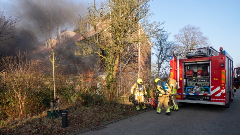 Brandweermannen bestrijden een woningbrand met een brandweerwagen en uitrusting, omgeven door rook.
