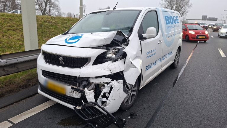 Een witte bestelwagen met zware schade aan de voorkant staat langs de weg na een ongeval.