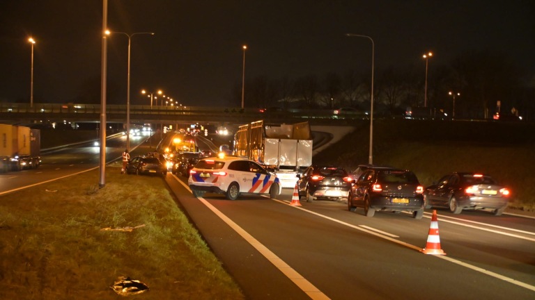 Verkeersopstopping op de snelweg 's nachts met politieauto en verkeerskegels die een rijstrook afsluiten.