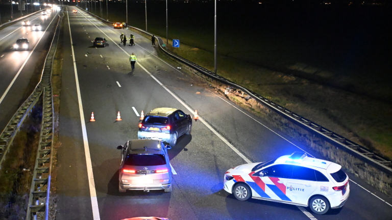 Politievoertuig met zwaailichten blokkeert een snelweg na een ongeval; meerdere auto's en agenten in actie.