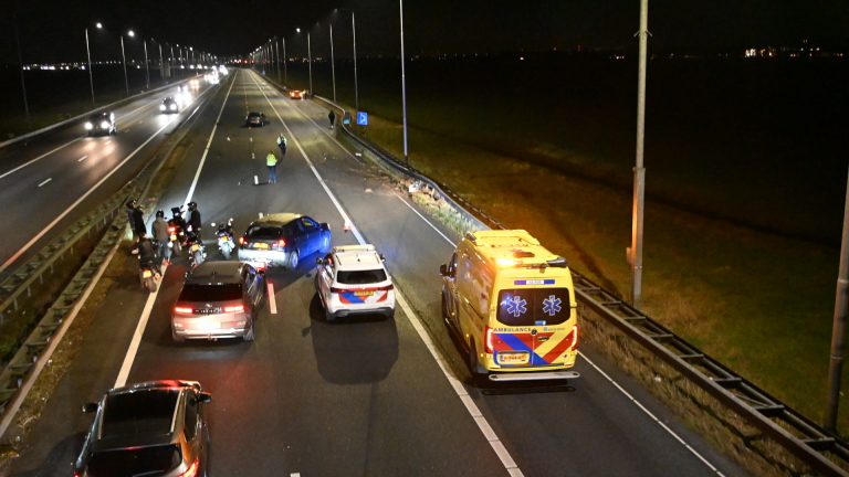 Politievoertuig met zwaailichten blokkeert een snelweg na een ongeval; meerdere auto's en agenten in actie.