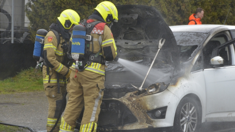 Brandweerlieden blussen een motorbrand van een beschadigde auto met brandweeruitrusting en -slangen.