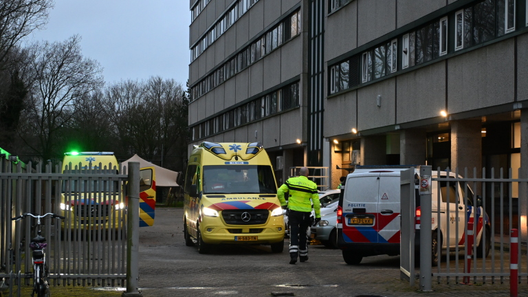 Politieagent en twee ambulances voor een flatgebouw met een politievoertuig op de achtergrond.