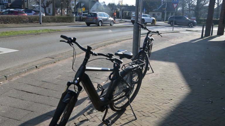Een geparkeerde fiets op de stoep voor een ambulance en verkeersbord met een politieagent op de achtergrond.