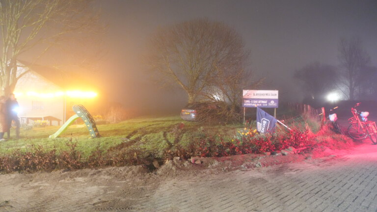Auto gebotst tegen een boom naast een reclamebord; de voorzijde is zwaar beschadigd, deuren staan open, het is nacht.
