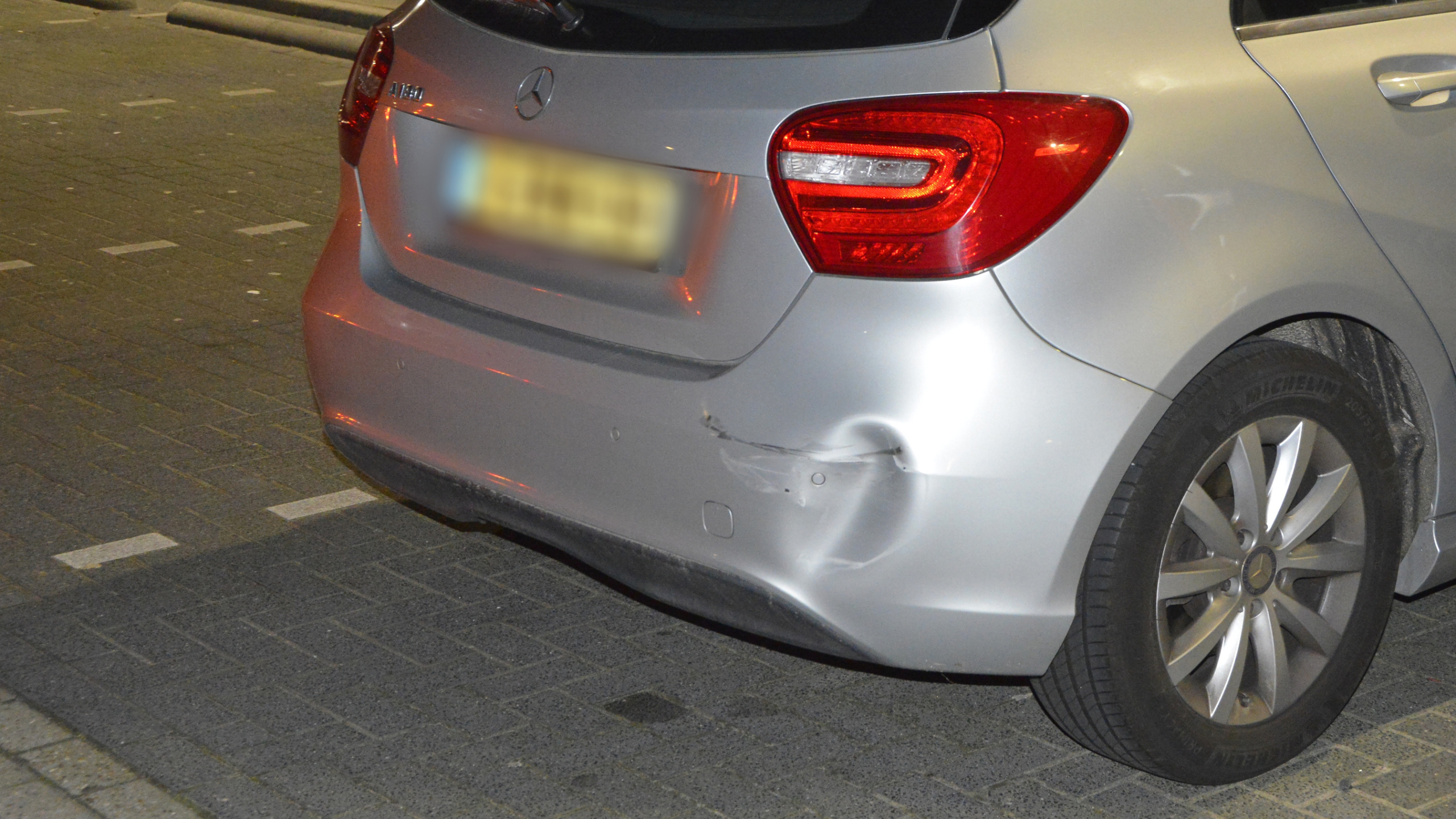 Twee auto's met schade op een parkeerplaats voor een MediaMarkt filiaal, omringd door mensen.