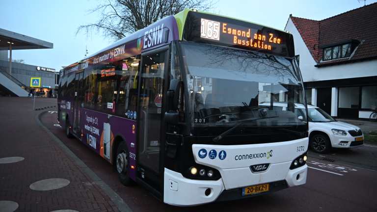 Een ambulance en politieauto staan met zwaailichten aan bij een kruising, omringd door omstanders en agenten.