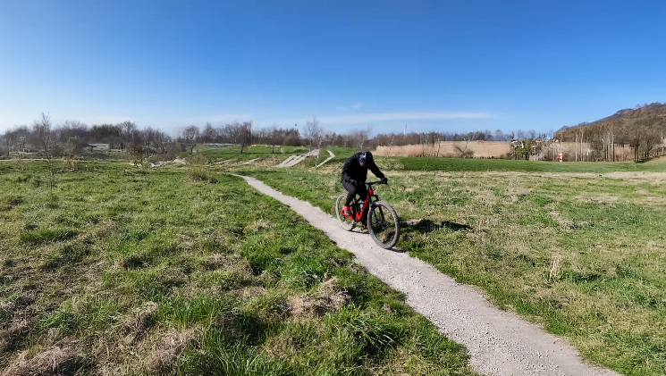 Een groep mountainbikers tilt hun fietsen op bij de ingang van MTB-Park van Luna, omgeven door bomen.