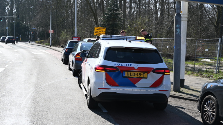 Twee auto's botsen op een weg met mensen die met een politieagent praten op de achtergrond.