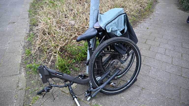 Zilverkleurige auto met een gebroken achterruit geparkeerd langs een rustige straat tegenover een huis.