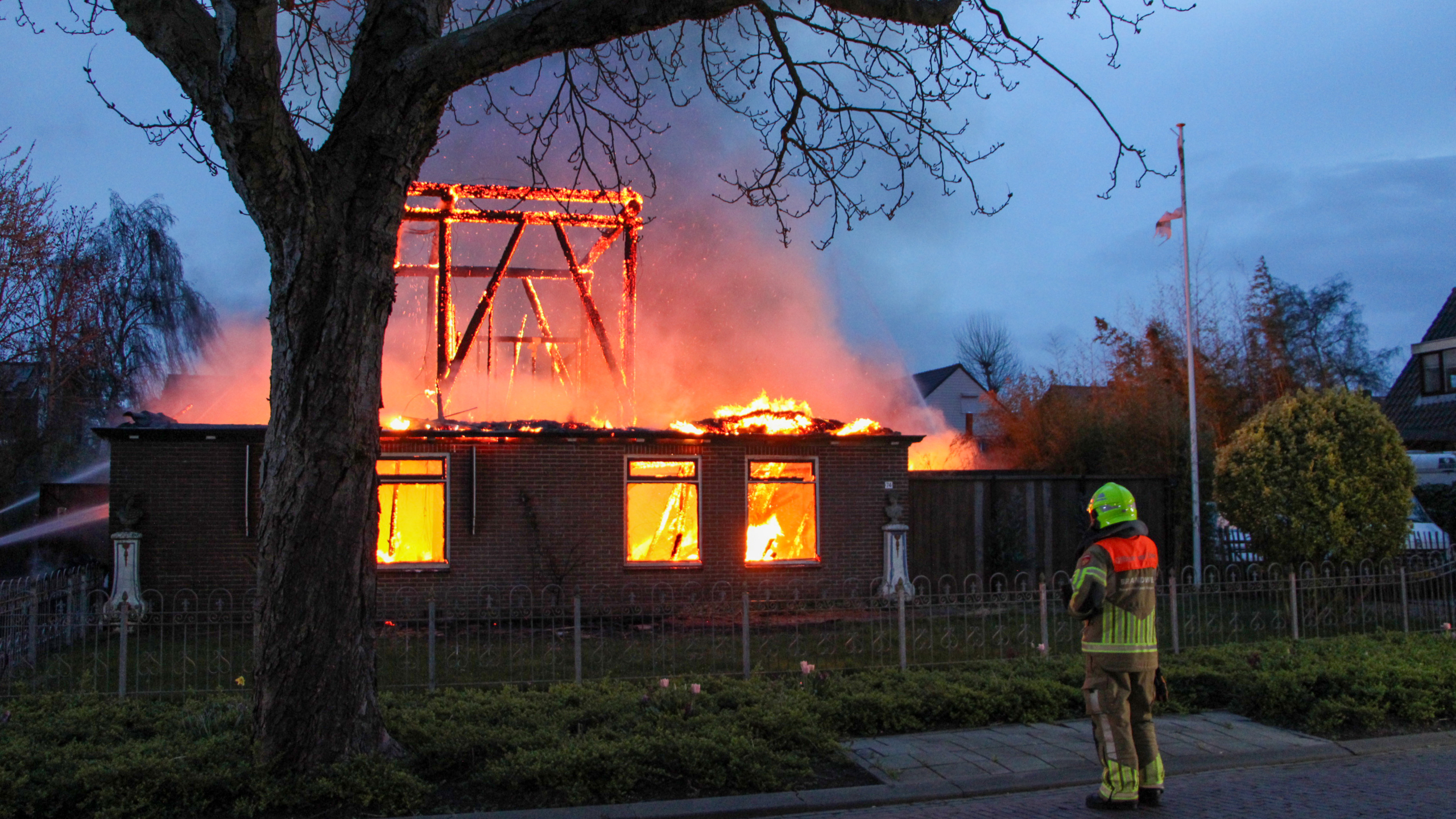 Brandweerlieden in volledige uitrusting bestrijden 's avonds een grote brand in een gebouw.