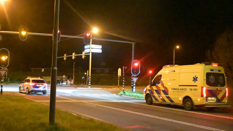 Een ambulance en een politiewagen bij een kruispunt met verkeerslichten 's nachts.