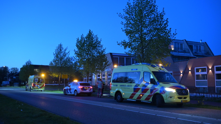 Agenten begeleiden een persoon naar een politieauto in het schemerlicht langs een rustige weg.