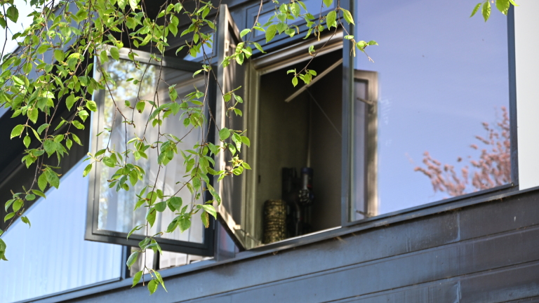 Brandweerlieden in beschermende uitrusting staan bij een brandweerwagen met uitgerolde slangen voor een modern huis.