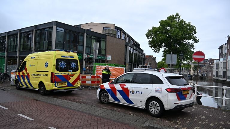 Een ambulance en politieauto staan geparkeerd bij een supermarkt in een straat met wegafzettingen en verbodsborden.
