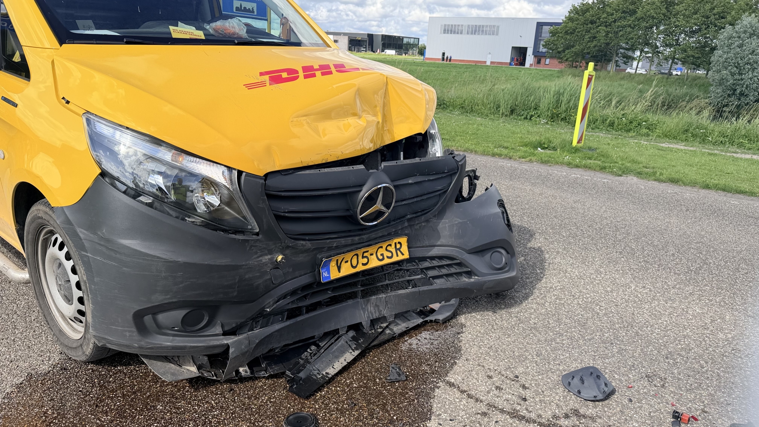 Gele DHL-bestelwagens met groene patronen staan langs de weg; politie en mensen kijken toe.
