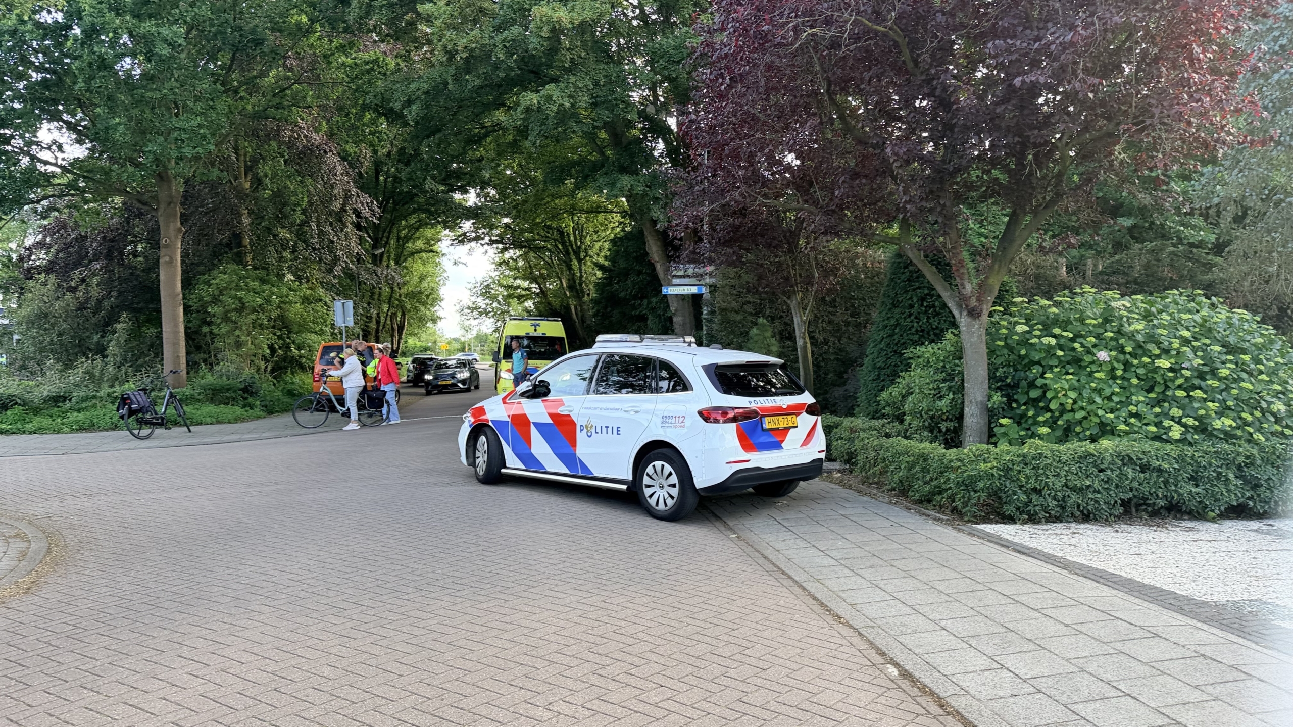Twee politieagenten staan bij een geparkeerde ambulance, terwijl een vrouw verderop aan de telefoon is.