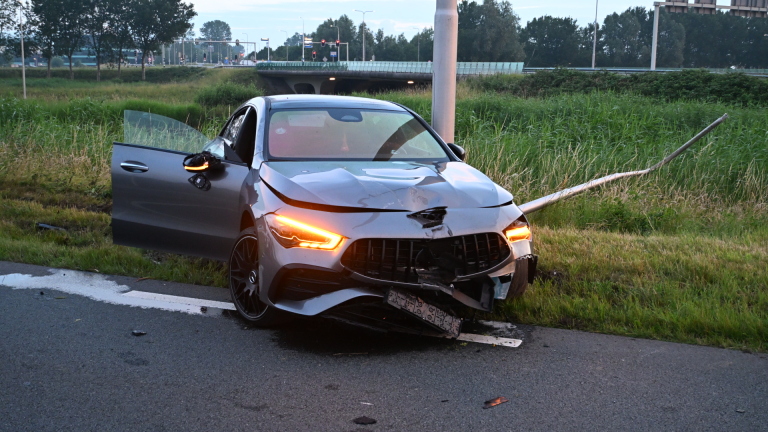 Een auto met ernstige schade aan de voorkant staat tegen een lantaarnpaal langs de weg.