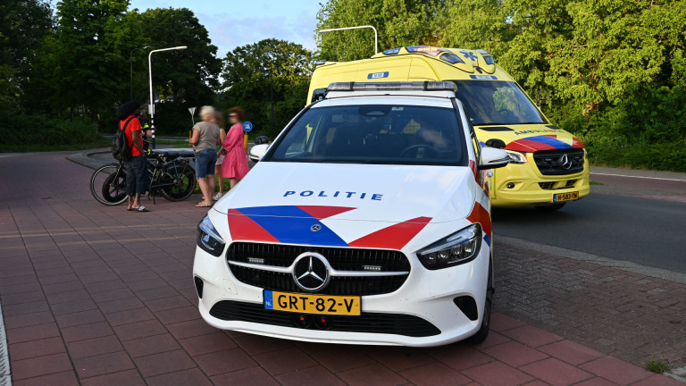 Politie- en ambulancevoertuigen staan op een weg nabij een groepje mensen met fietsen.
