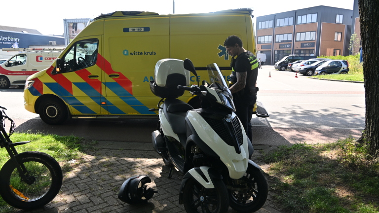 Een politiewagen naast een ambulance met een witte driewielige scooter en een helm op de stoep.