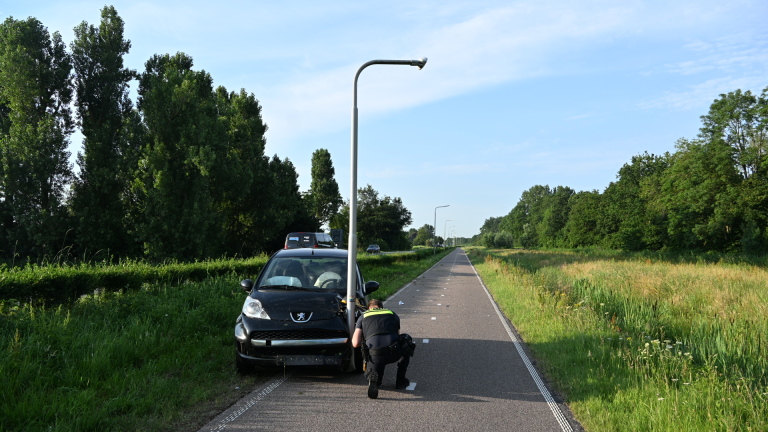 Auto gebotst tegen lantaarnpaal op rustige weg, met agent die schade inspecteert.