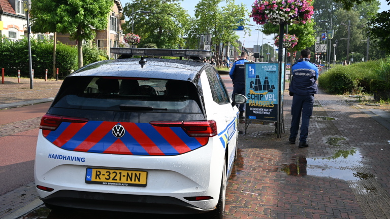 Een beschadigd gebouw met rode pilaren en een ingestort dak, naast een straat met een bestelbus en een reclamebord.