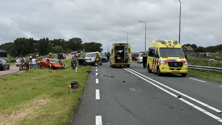 Verkeersongeval op een snelweg met betrokken auto's, brandweerlieden en twee ambulances aanwezig, omstanders kijken toe.