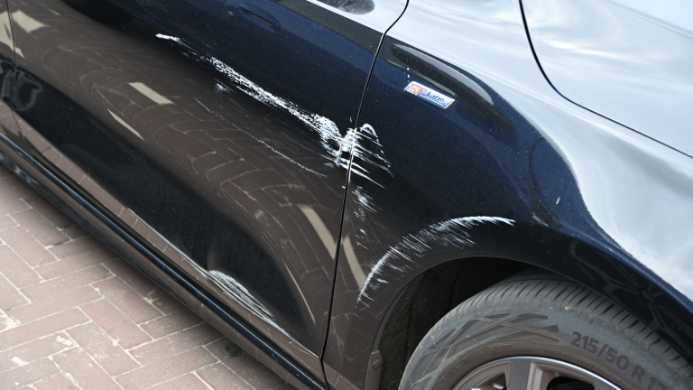 Een politieagent meet een kras op de zijkant van een witte auto op een parkeerplaats.