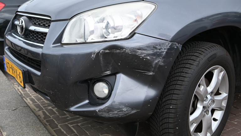 Een politieagent meet een kras op de zijkant van een witte auto op een parkeerplaats.
