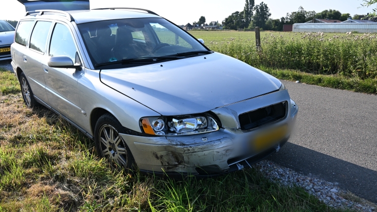 Blauwe auto met zware schade aan de linker voorkant staat op een kruispunt, met het rechterportier open