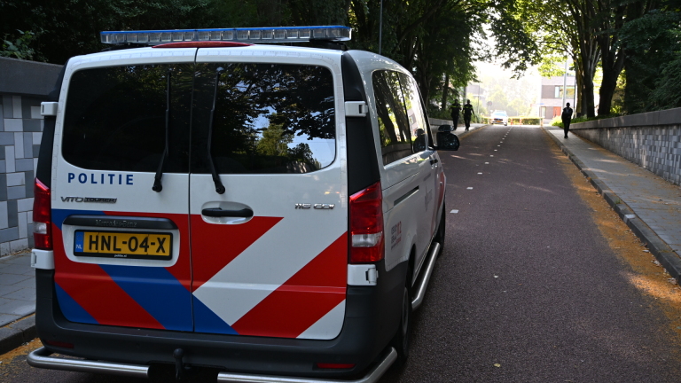 Politieagent loopt in een tunnel langs twee gele ambulances op een fietspad, met daglicht en bomen op de achtergrond