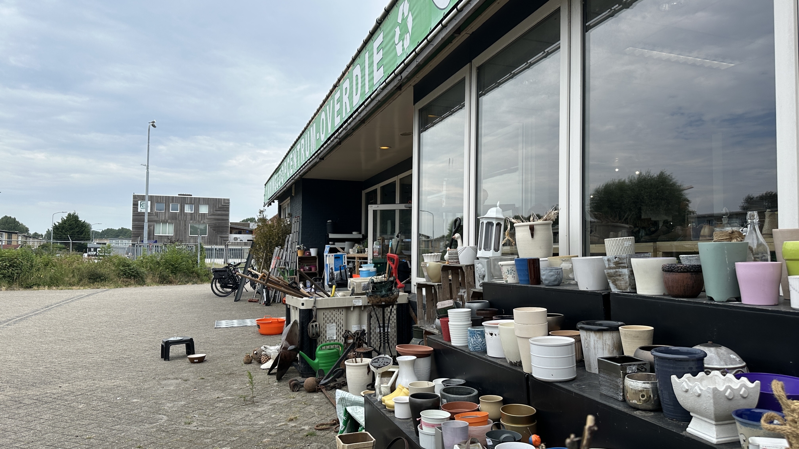 Industrieel gebouw met bord Kringloopcentrum Overdie, met geparkeerde auto’s en een lantaarnpaal langs de weg