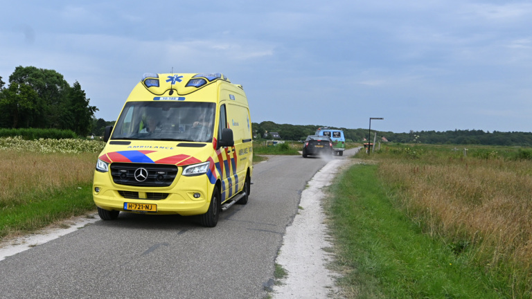 Gele ambulancebus van Witte Kruis met open schuifdeur, terwijl een hulpverlener spullen pakt naast een huis