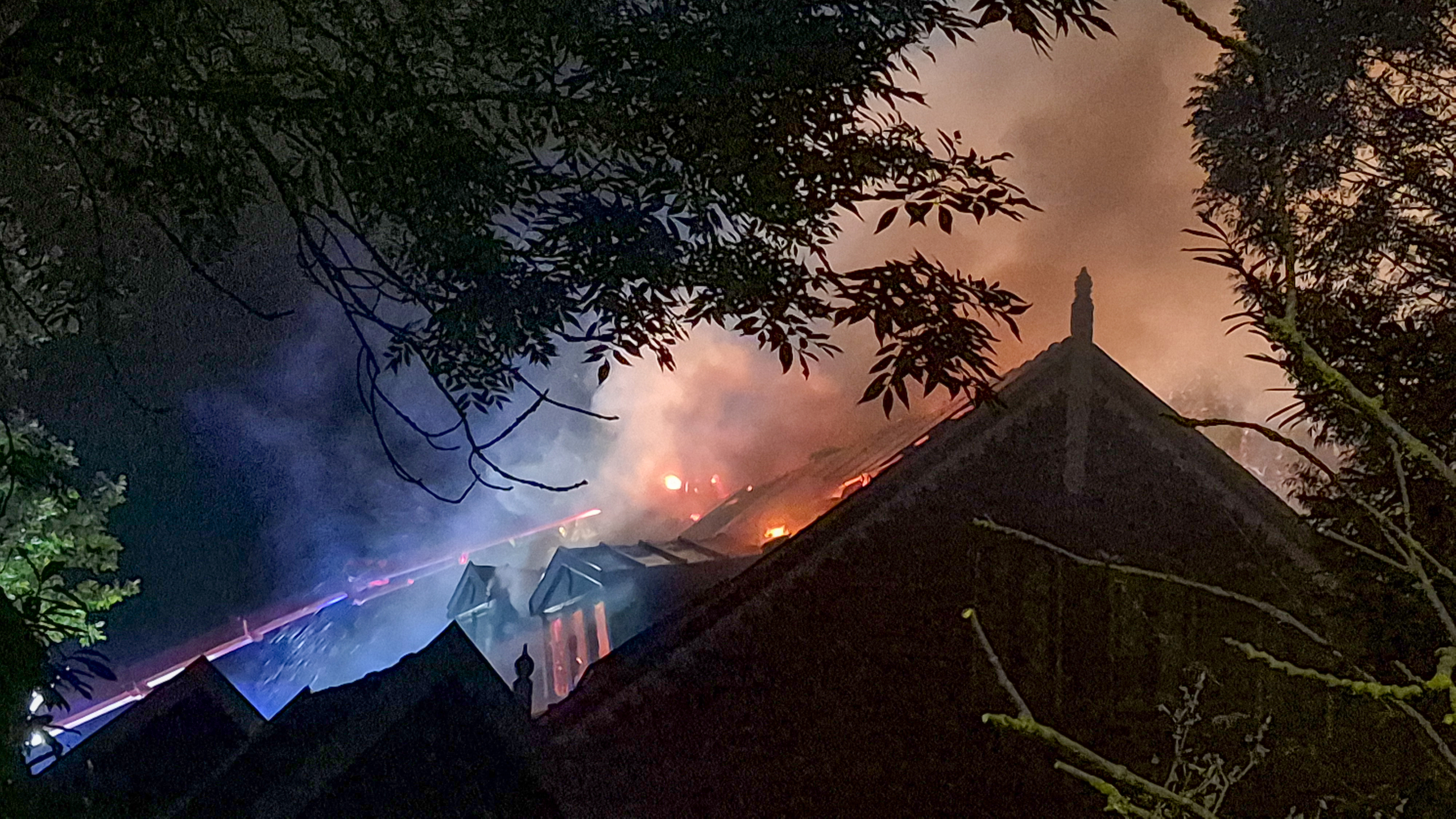 Brandweerwagen met hoogwerker bij uitslaande dakbrand van woning in de nacht, met rook, vlammen en brandweerlieden