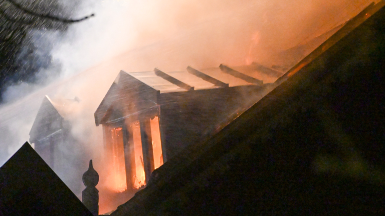 Brandweerwagen met hoogwerker bij uitslaande dakbrand van woning in de nacht, met rook, vlammen en brandweerlieden