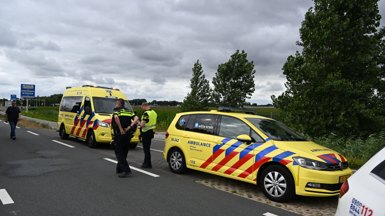 Rode auto half onder water in een rivier, met de voorkant en voorruit zichtbaar naast een begroeide oever