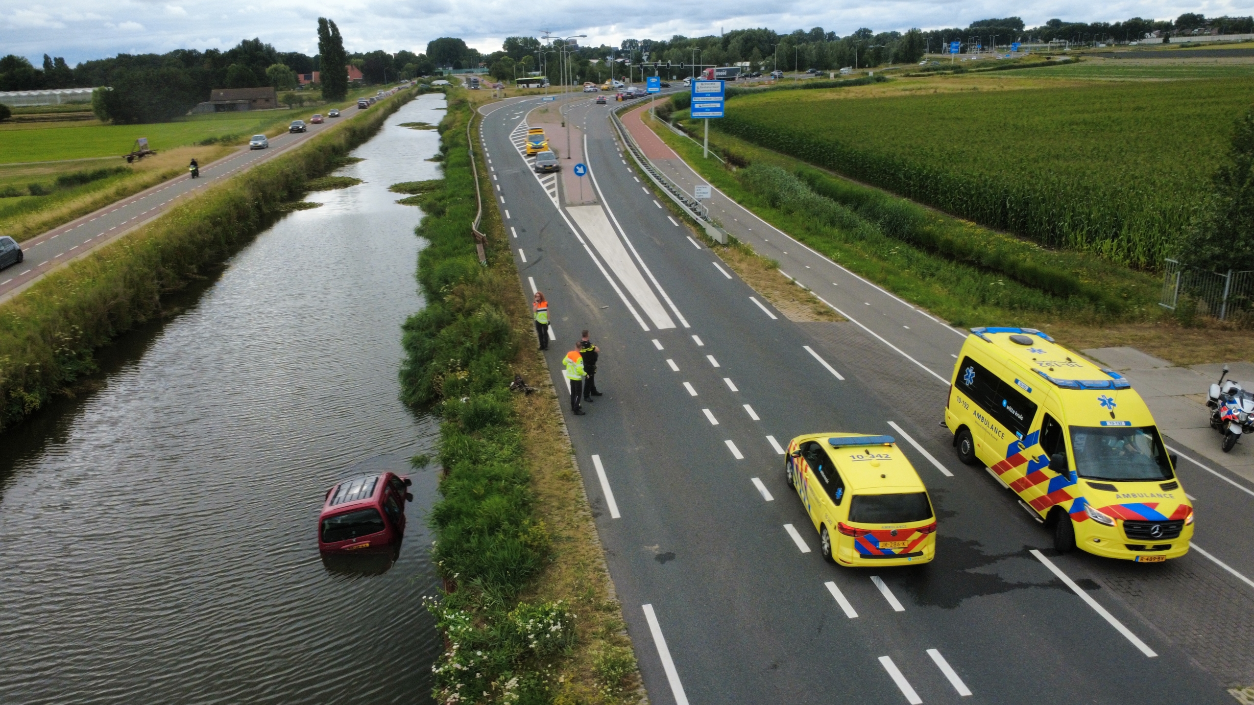 Rode auto half onder water in een rivier, met de voorkant en voorruit zichtbaar naast een begroeide oever