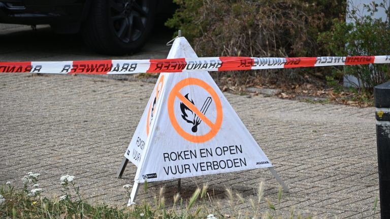 Brandweerlieden in beschermende kleding bij een woning met garage, één loopt naar de groep bij een auto