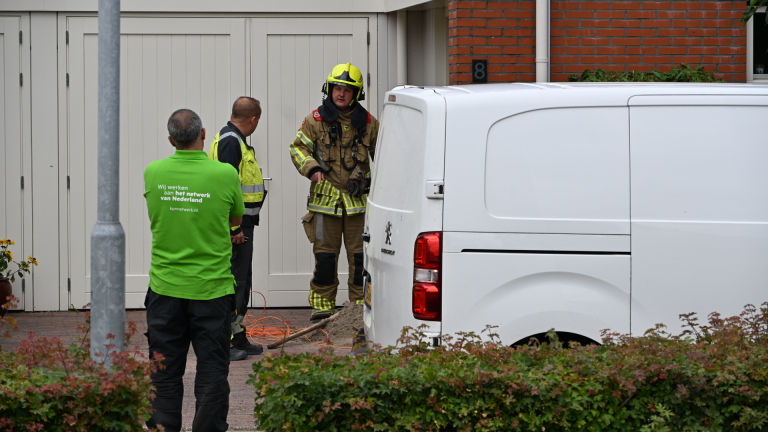 Brandweerlieden in beschermende kleding bij een woning met garage, één loopt naar de groep bij een auto
