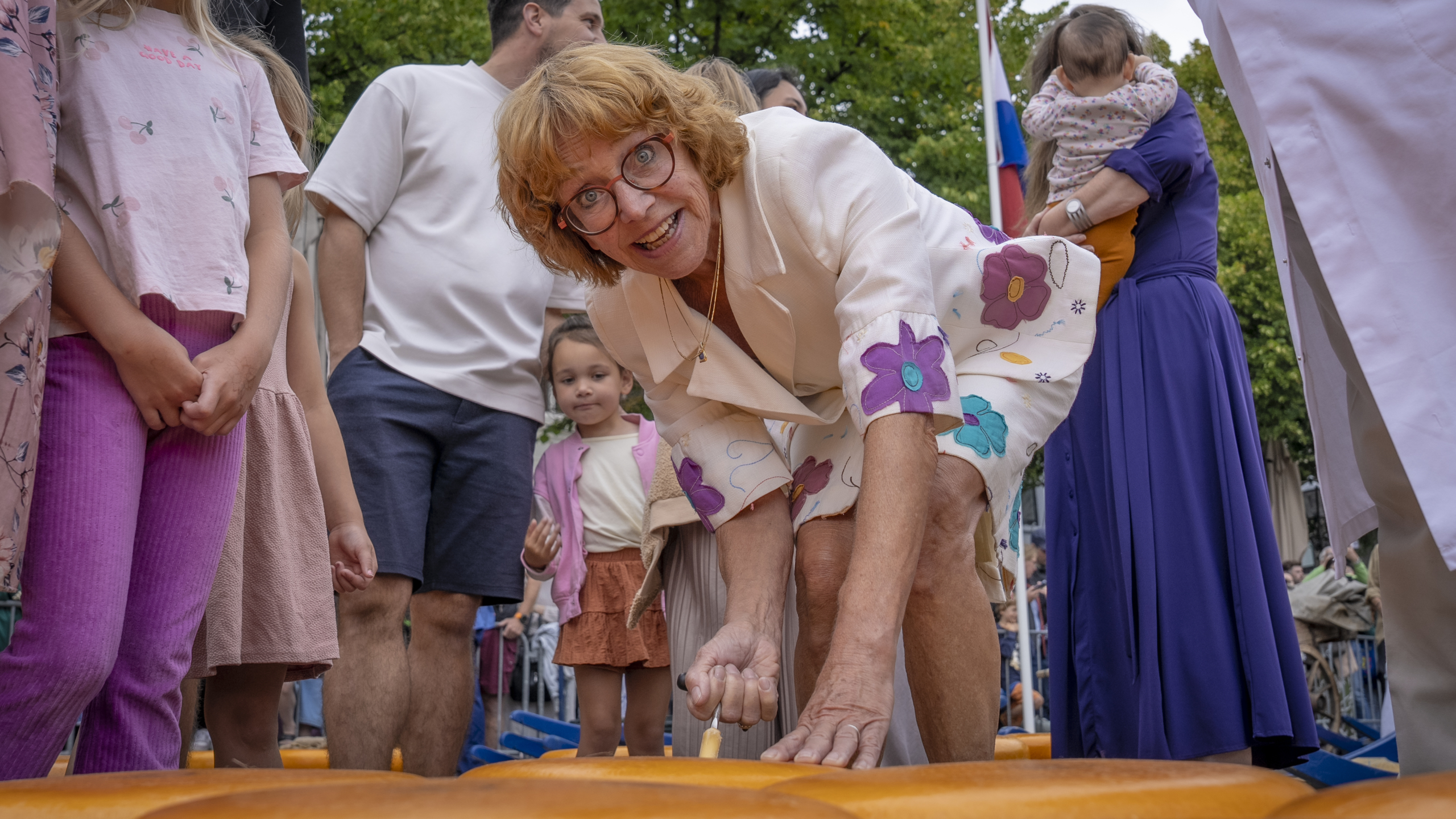 Groepsfoto van mensen in traditionele Nederlandse klederdracht met kleurrijke hoeden voor een bakstenen gebouw