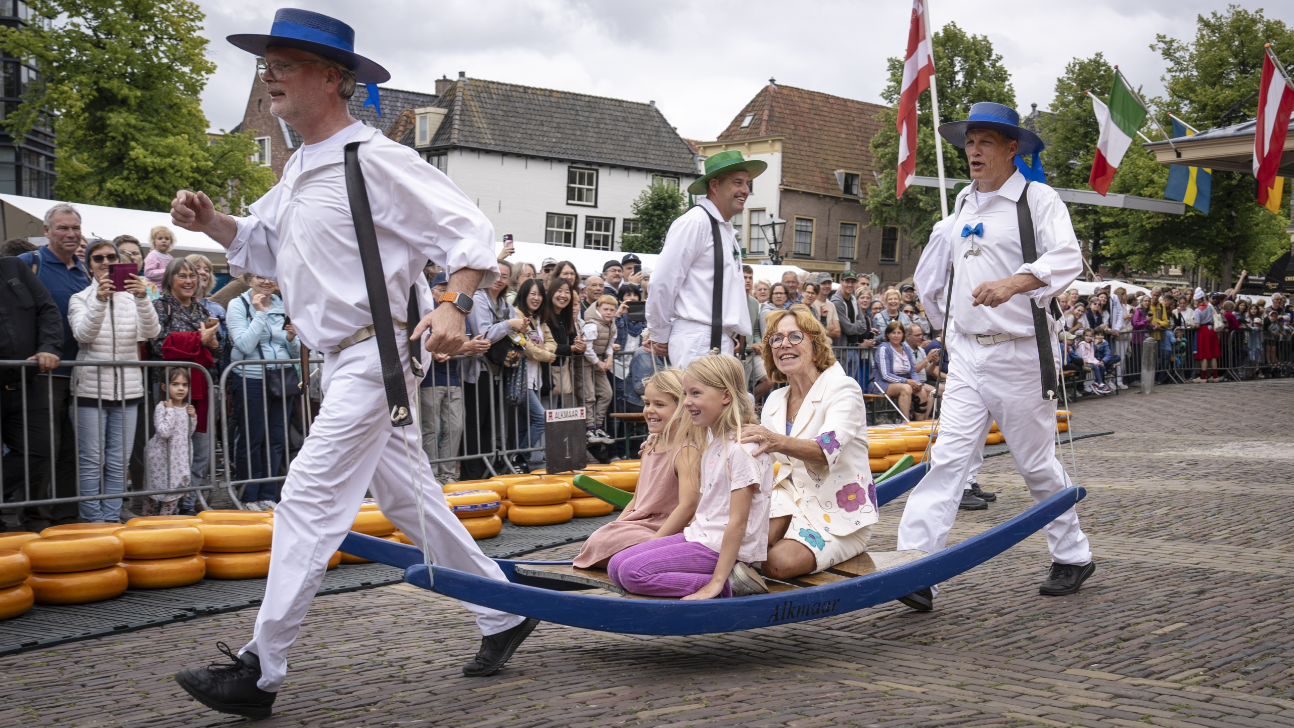 Groepsfoto van mensen in traditionele Nederlandse klederdracht met kleurrijke hoeden voor een bakstenen gebouw