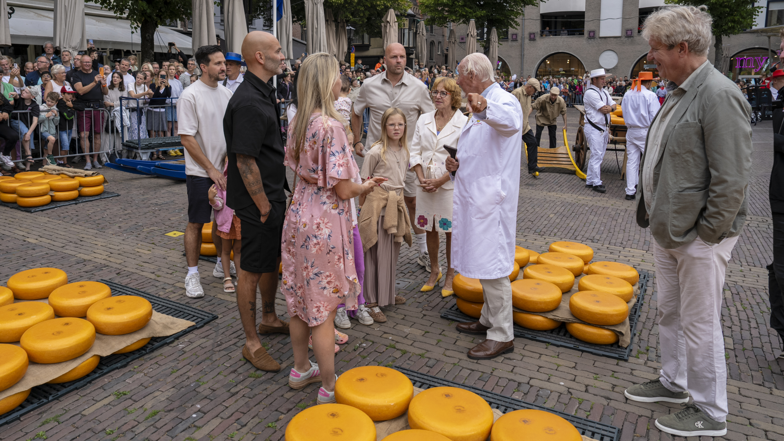 Groepsfoto van mensen in traditionele Nederlandse klederdracht met kleurrijke hoeden voor een bakstenen gebouw