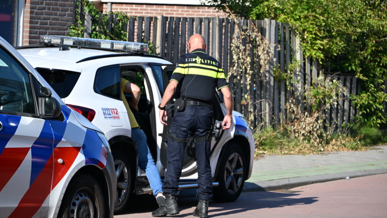 Politieauto en ambulance geparkeerd in een woonstraat met huizen en bomen, met meerdere auto’s langs de weg