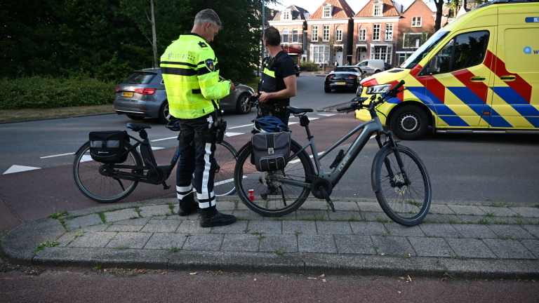 Ambulance en politiemotor blokkeren een kruispunt; agenten staan bij een politieauto en wegwijzers naar Ring en Centrum