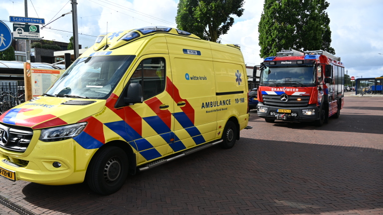 Twee brandweerlieden lopen over een tramhalte richting poortjes; rechts staat een politiemotor geparkeerd